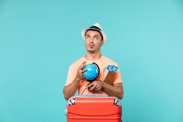 Photo gratuit homme en vacances tenant un petit globe avec des billets d'avion sur bleu