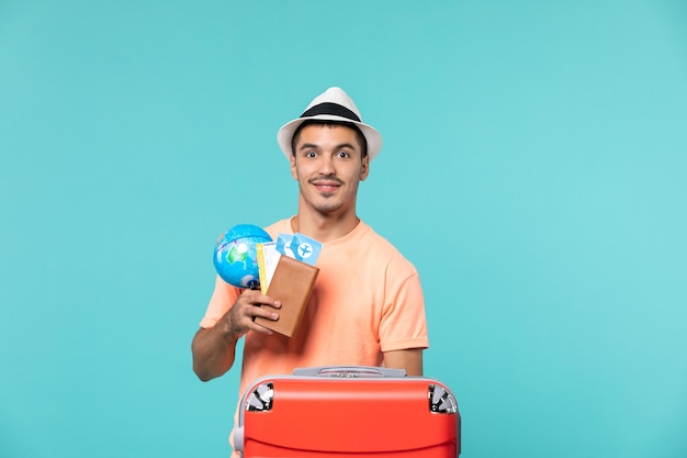 Photo gratuite homme en vacances tenant un petit globe avec des billets d'avion sur bleu