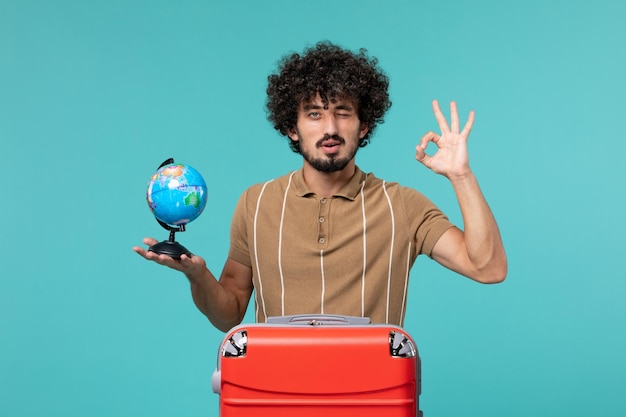 homme en vacances tenant un petit globe avec un sac rouge sur bleu