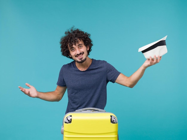 homme en vacances tenant son chapeau sur bleu