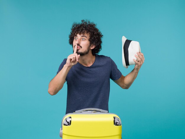 homme en vacances tenant son chapeau sur bleu