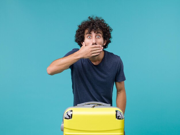 homme en vacances avec valise jaune et expression surprise sur bleu