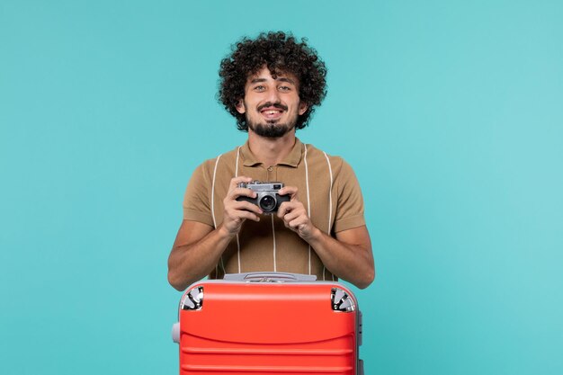 homme en vacances avec valise rouge prenant des photos avec appareil photo sur bleu