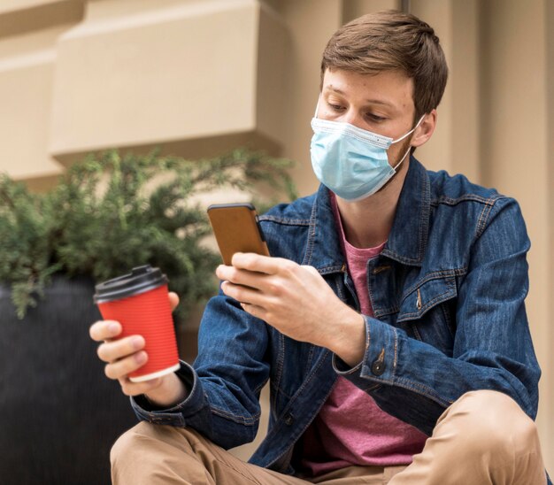 Homme vérifiant son téléphone à l'extérieur avec un masque facial sur