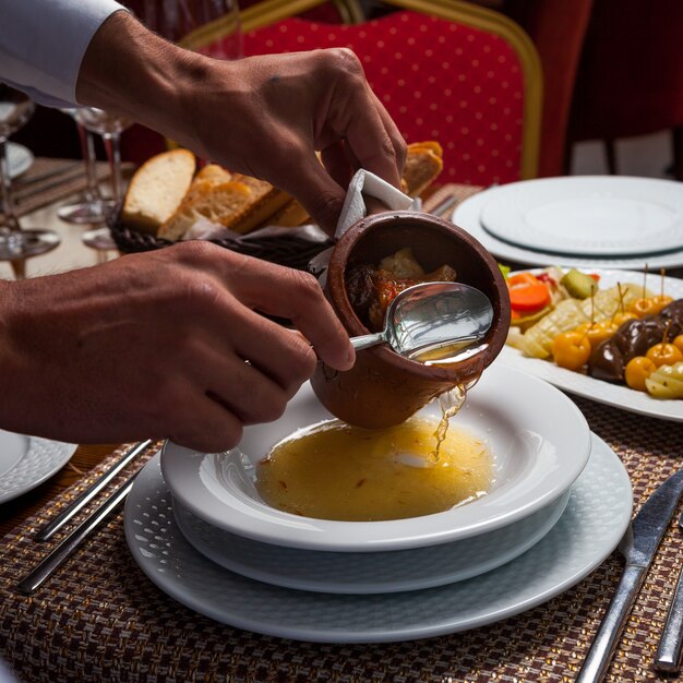 Homme, Verser, délicieux, oriental, pois, soupe, viande, plaque, bois, table vue grand angle.