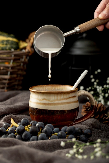 Homme, verser le lait dans une tasse à café brune avec des raisins sur un drap gris