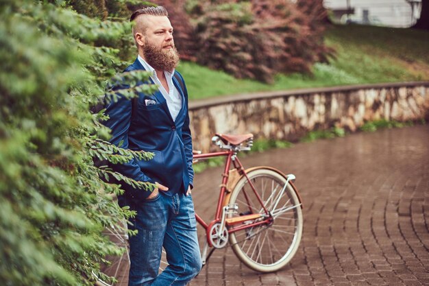 Homme vêtu de vêtements décontractés, debout avec un vélo rétro dans un parc de la ville.