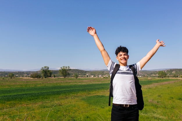 Homme voyageur joyeux avec la main levée debout dans le champ vert