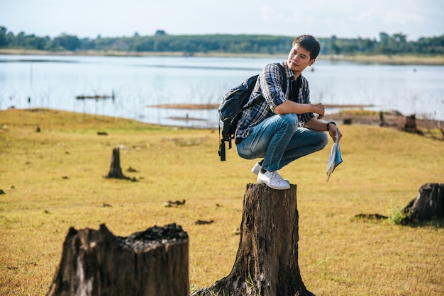 Un homme voyageur avec un sac à dos portant une carte et assis sur une souche d'arbre.