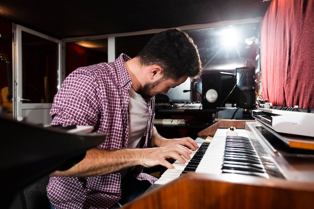 Homme vue de côté jouant du clavier en studio