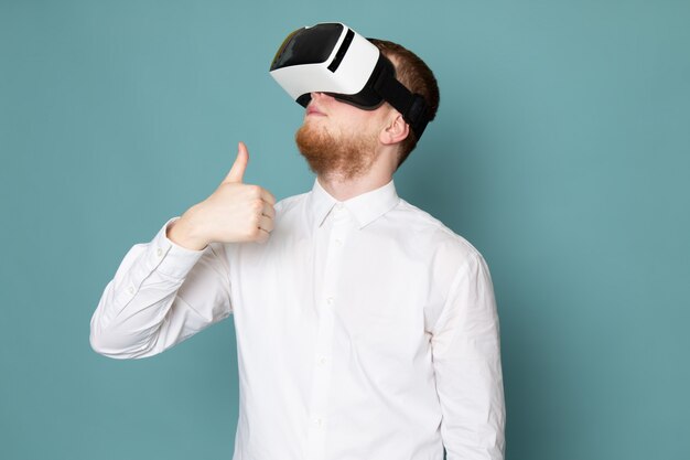 Un homme vue de face à l'aide de vr en t-shirt blanc sur le bureau bleu