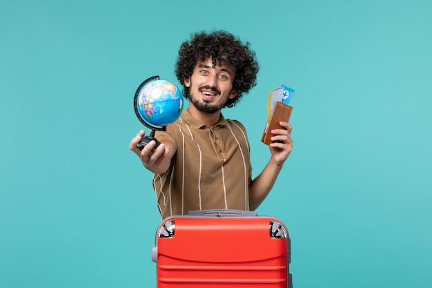 Homme vue de face en vacances tenant un globe et un billet sur bleu