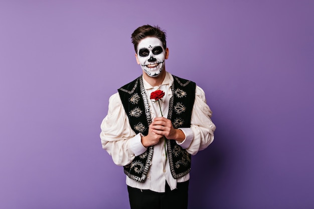 Homme zombie joyeux en chemise blanche posant avec fleur. Photo intérieure d'un mec caucasien blithesome avec rose rouge.