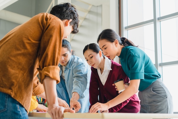 Hommes d'affaires et femmes d'affaires asiatiques réunissant des idées de remue-méninges sur l'application de planification de conception Web créative et le développement de la mise en page de modèle pour un projet de téléphone mobile travaillant ensemble dans un petit bureau.