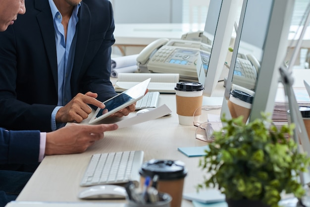 Hommes d'affaires méconnaissables assis au bureau et regardant ensemble la tablette et le document