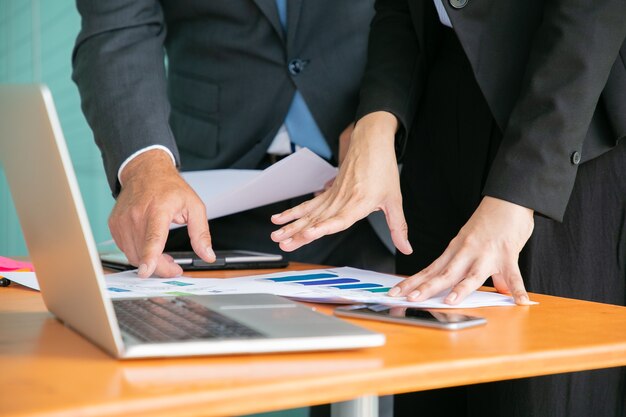 Hommes d'affaires méconnaissables étudiant les statistiques et tenant des papiers avec les mains