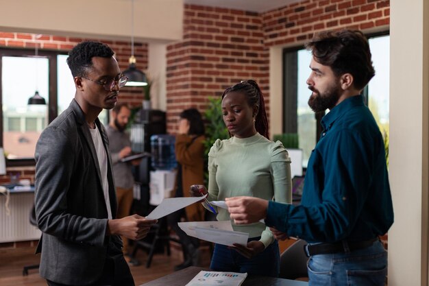 Des hommes d'affaires multiethniques discutent de la collaboration commerciale après avoir analysé les statistiques marketing. Femme indépendante expliquant la stratégie de l'entreprise travaillant sur un projet financier dans un bureau de mur de briques