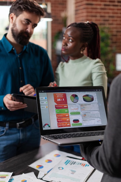 Photo gratuite des hommes d'affaires multiraciaux analysant le chiffre d'affaires de l'entreprise discutant de la collaboration commerciale tout en travaillant dans un bureau de démarrage de mur de briques. une équipe multiethnique réfléchit à des idées pour un projet marketing