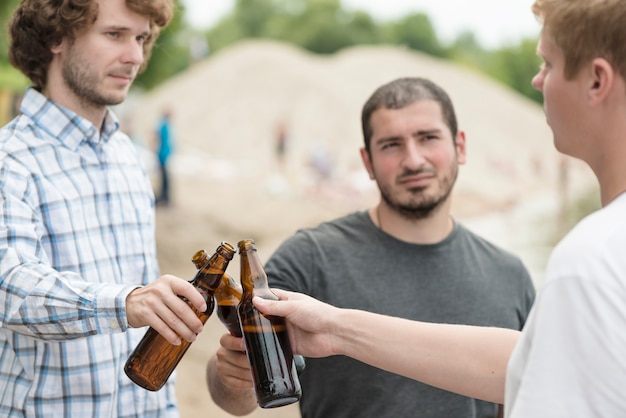 Photo gratuite hommes clink bouteilles sur la plage