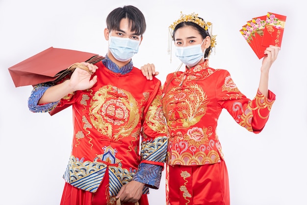 Les hommes et les femmes portant Qipao et portant des masques portant des sacs en papier pour faire du shopping avec enveloppe rouge