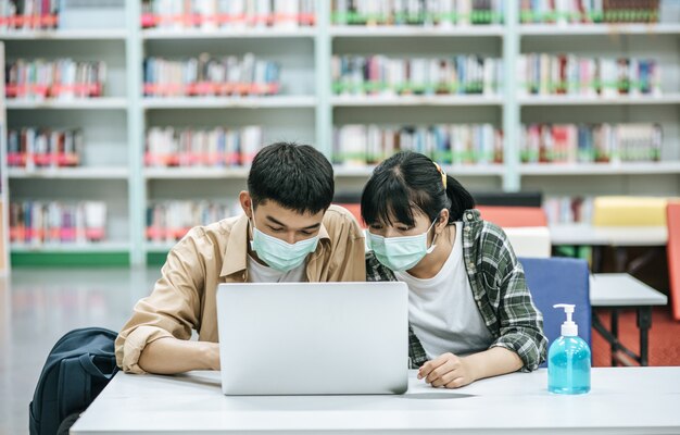 Les hommes et les femmes portent des masques et utilisent un ordinateur portable pour rechercher des livres dans la bibliothèque.