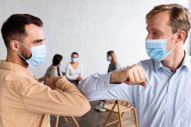 Hommes avec des masques médicaux lors d'une séance de thérapie de groupe faisant le salut du coude