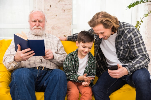 Des hommes multigénérationnels passant du temps ensemble à parcourir des livres et des smartphones