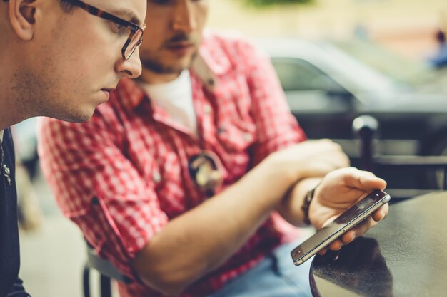 Les hommes partagent des nouvelles, des photos, des vidéos sur le smartphone. Un homme montre un ami une application dans un téléphone portable. Amis avec un smartphone, la technologie.