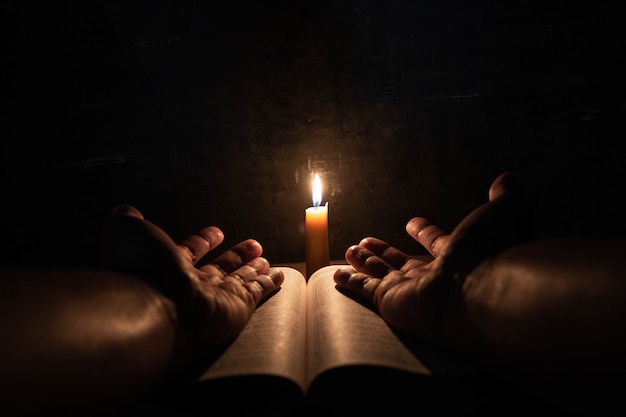 Photo gratuite les hommes priant sur la bible à la lumière des bougies se concentrent sélectivement.