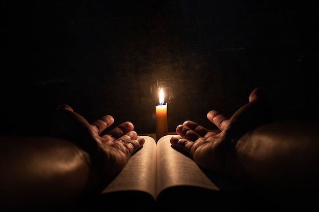 Les hommes priant sur la Bible à la lumière des bougies se concentrent sélectivement.