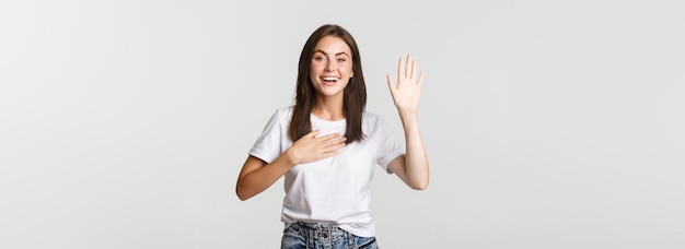 Honnête fille mignonne souriante disant la vérité levant la main pour faire une promesse