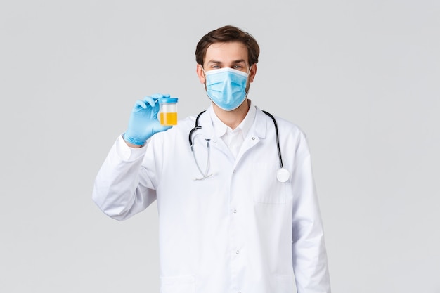 Hôpital, travailleurs de la santé, concept de traitement covid-19. médecin optimiste souriant dans des gommages blancs, portez un masque médical et des gants, technicien de laboratoire montrant un récipient avec un échantillon d'urine.