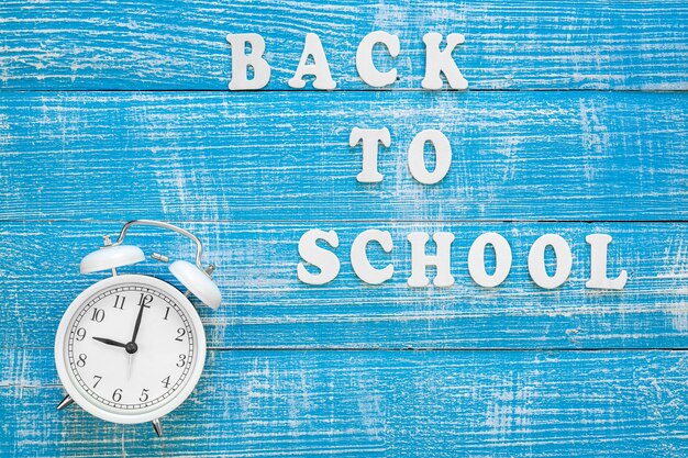 Horloge réveil et inscription de retour à l'école sur un fond en bois vue du haut