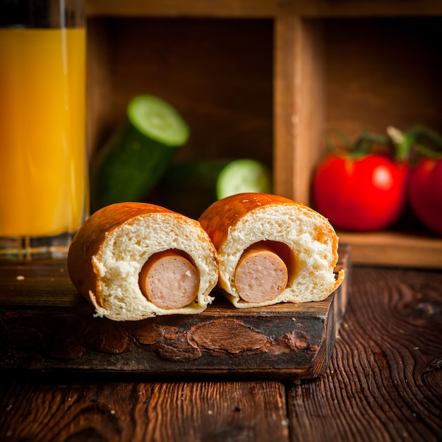 Hot-Dog avec jus d'orange et concombres et tomates en planche de bois