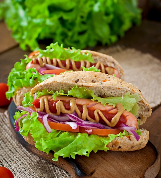 Hot-dog avec moutarde ketchup et laitue sur table en bois.