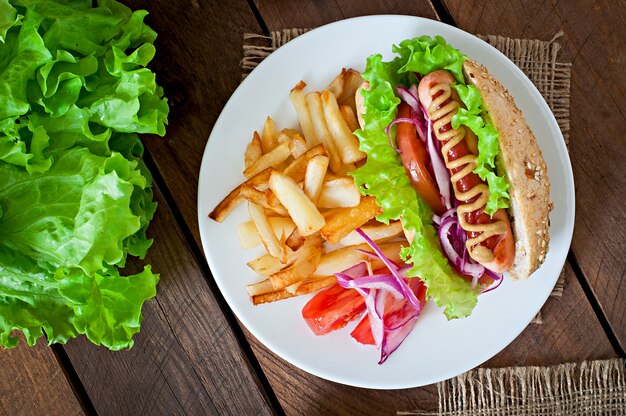 Hot-dog avec moutarde ketchup et laitue sur table en bois.