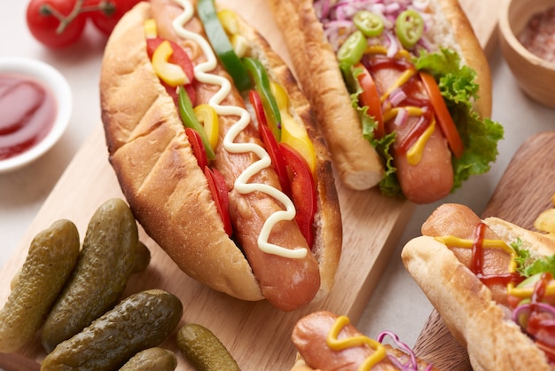 Hot dog tout bœuf grillé gastronomique avec accompagnements et frites. Des hot dogs délicieux et simples avec de la moutarde, du poivre, de l'oignon et des nachos. Hot-dogs entièrement chargés de garnitures assorties sur une planche à pagaie.