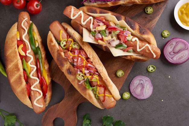 Hot dog tout bœuf grillé gastronomique avec accompagnements et frites. Des hot dogs délicieux et simples avec de la moutarde, du poivre, de l'oignon et des nachos. Hot-dogs entièrement chargés de garnitures assorties sur une planche à pagaie.