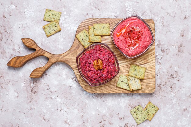 Houmous de betterave sur une planche à découper avec des biscuits salés sur une surface claire