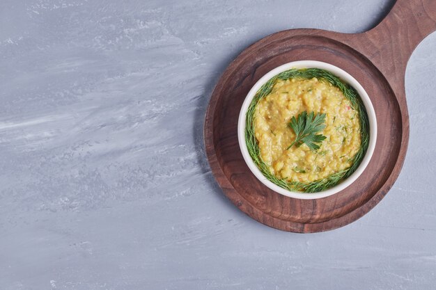 Houmous dans une tasse blanche avec des herbes sur une planche de bois.