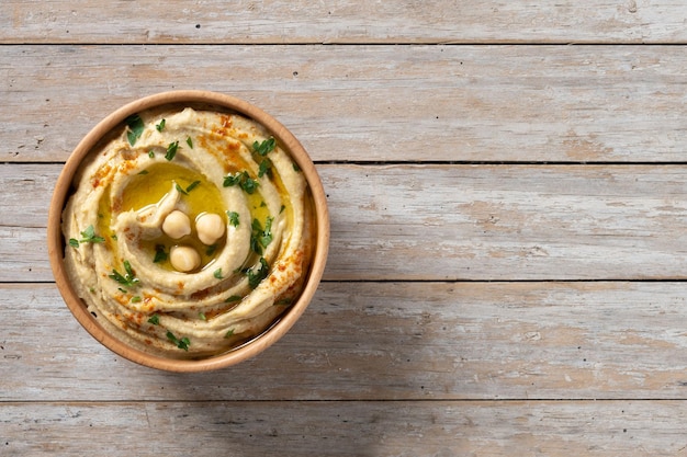 Houmous de pois chiches dans un bol en bois garni de paprika persil et d'huile d'olive sur table en bois