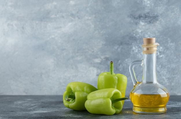 Huile saine fraîche avec des poivrons verts biologiques sur fond gris.