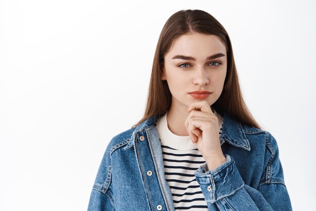 Hum très intéressant. Une fille intelligente réfléchie touche le menton, regarde la caméra avec un visage pensif concentré, réfléchit, prend une décision, choisit quelque chose, se tient sur fond blanc