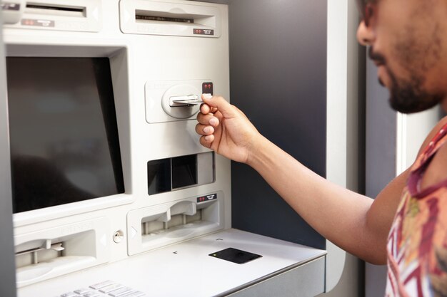 Humain et technologie. Homme à la peau sombre utilisant ATM. La main du black insérant une carte bancaire en plastique dans un distributeur de billets ou un guichet automatique