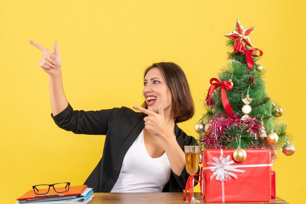 L'humeur du nouvel an avec une belle femme d'affaires pointant joyeusement quelque chose et assis à une table dans le bureau