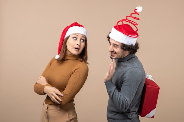 L'humeur du nouvel an avec un couple charmant drôle portant des chapeaux de père Noël rouge se parlant les uns aux autres sur le gris