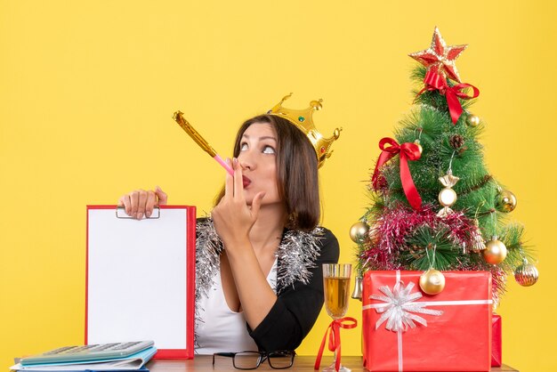 L'humeur du nouvel an avec une dame charmante surprise réfléchie en costume avec couronne tenant un document dans le bureau sur jaune isolé