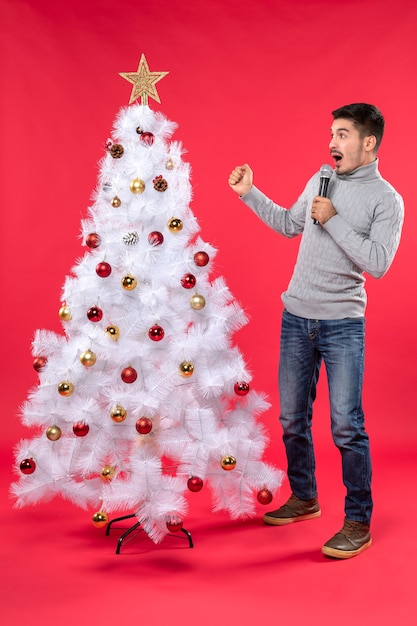 L'humeur du nouvel an avec un gars positif habillé en jeans debout près de l'arbre de Noël décoré