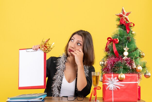 L'humeur du nouvel an avec surprise charmante dame en costume tenant le document et la couronne au bureau sur jaune isolé