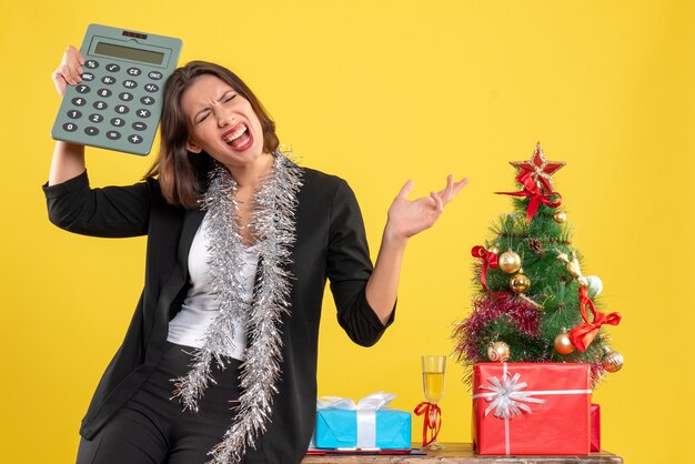 L'humeur de Noël avec une belle dame tendue debout dans le bureau et tenant la calculatrice au bureau sur jaune